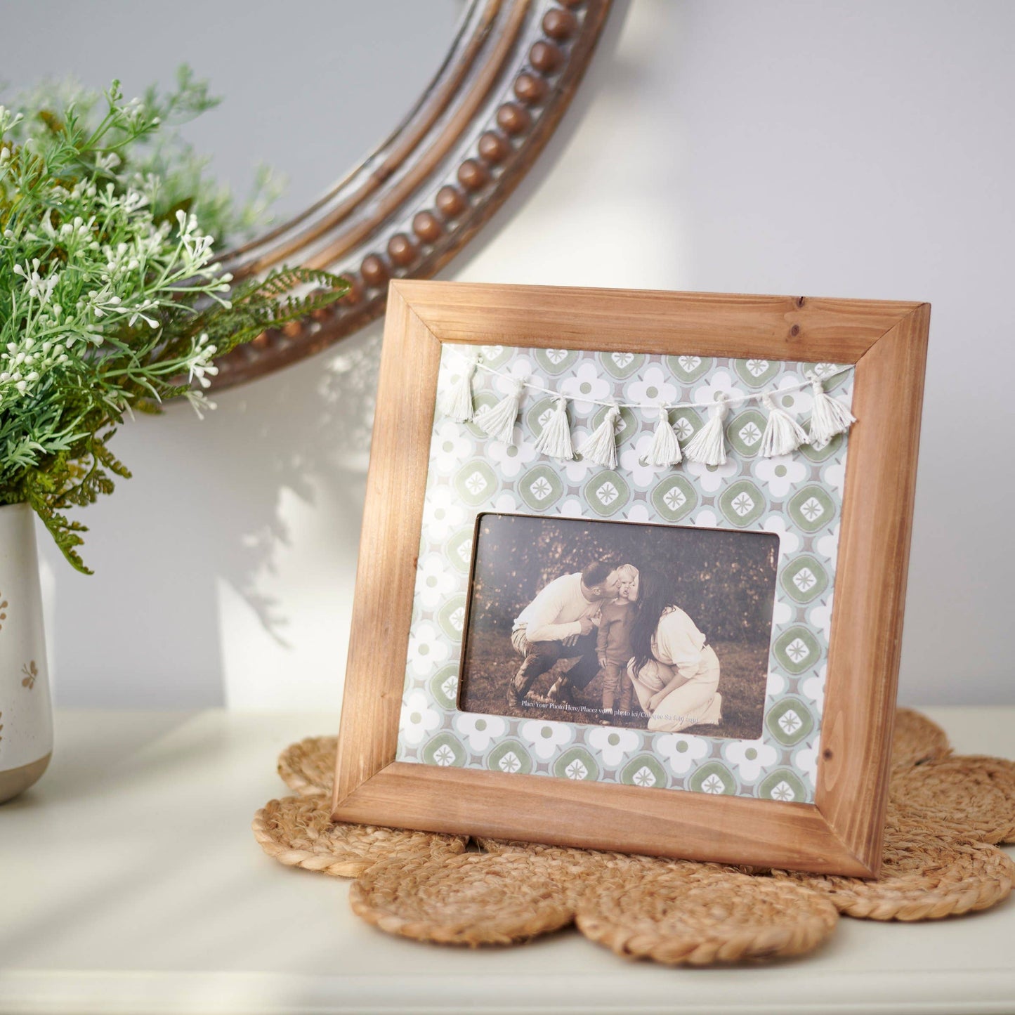 Wooden picture frame with a decorative mat and photo on a surface with a plant and mirror in the background.